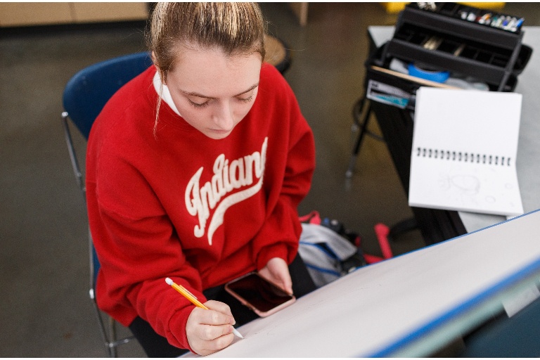Female student in an Indiana University sweatshirt drawing on a large piece of paper in IUPUI's Herron School of Art